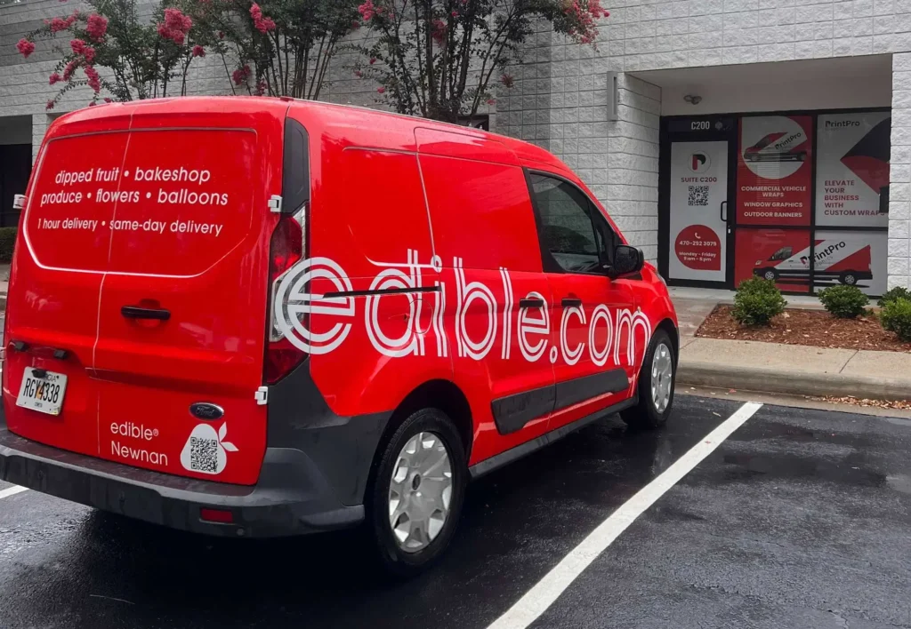 Red delivery van with "edible.com" branding parked outside a building. Text on van promotes fruit, bakery, and flower delivery services. Overcast day.